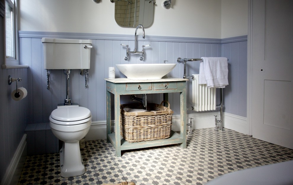 Mid-sized traditional bathroom in Sussex with furniture-like cabinets, distressed cabinets, a claw-foot tub, a shower/bathtub combo, a two-piece toilet, cement tile, mosaic tile floors, multi-coloured walls, a vessel sink and gray tile.