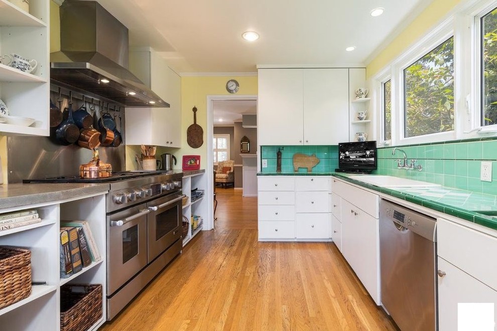 Inspiration for a small country galley separate kitchen in Los Angeles with a single-bowl sink, open cabinets, white cabinets, tile benchtops, green splashback, porcelain splashback, stainless steel appliances, medium hardwood floors, no island, brown floor and green benchtop.