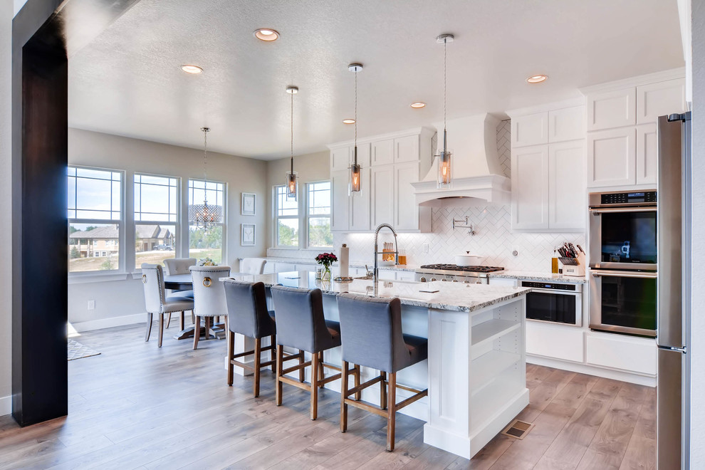 Inspiration for a large modern galley eat-in kitchen in Denver with a farmhouse sink, shaker cabinets, white cabinets, quartz benchtops, white splashback, subway tile splashback, stainless steel appliances, medium hardwood floors, with island, brown floor and multi-coloured benchtop.