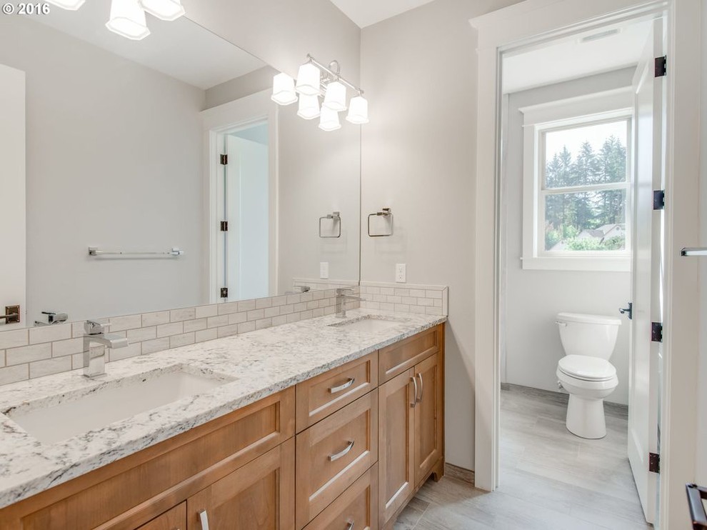 Photo of an expansive arts and crafts kids bathroom in Portland with shaker cabinets, light wood cabinets, an undermount tub, a shower/bathtub combo, a one-piece toilet, gray tile, ceramic tile, grey walls, ceramic floors, an undermount sink, engineered quartz benchtops, grey floor, a hinged shower door and white benchtops.