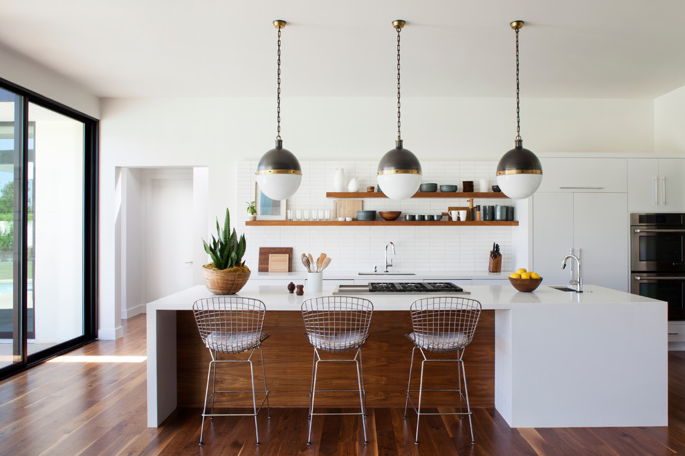 Inspiration for a mid-sized midcentury l-shaped open plan kitchen in Los Angeles with a single-bowl sink, flat-panel cabinets, white cabinets, quartz benchtops, white splashback, ceramic splashback, panelled appliances, medium hardwood floors and with island.