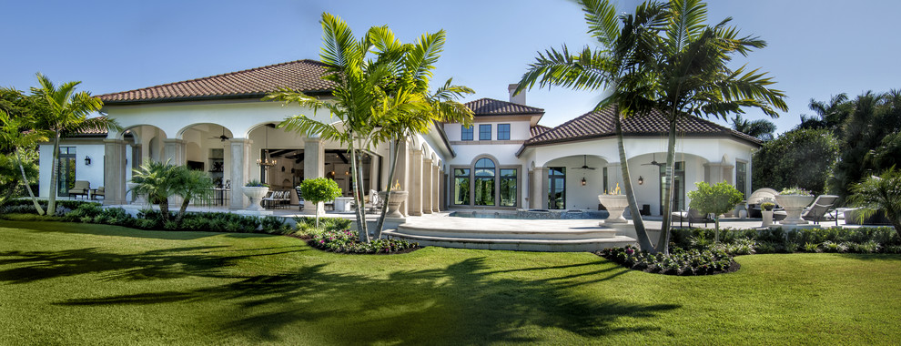 This is an example of a large mediterranean one-storey stucco beige house exterior in Miami with a hip roof and a tile roof.