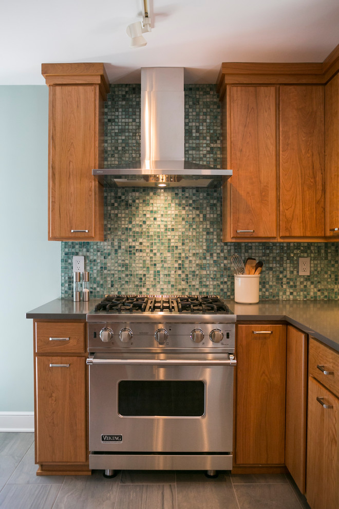 Photo of a small midcentury l-shaped separate kitchen in Other with an undermount sink, flat-panel cabinets, medium wood cabinets, solid surface benchtops, green splashback, glass tile splashback, stainless steel appliances, porcelain floors, no island and grey benchtop.