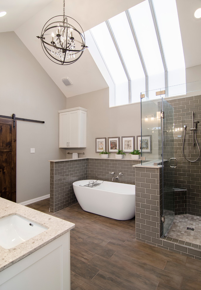 Transitional master bathroom in Dallas with shaker cabinets, white cabinets, a freestanding tub, gray tile, grey walls, medium hardwood floors, an undermount sink and a hinged shower door.