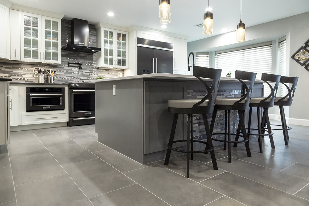 Example of a mid-sized transitional l-shaped porcelain tile and gray floor open concept kitchen design in Phoenix with an undermount sink, shaker cabinets, white cabinets, quartz countertops, gray backsplash, glass tile backsplash, black appliances, an island and gray countertops