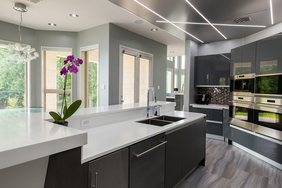 Design ideas for a large contemporary u-shaped open plan kitchen in Dallas with a farmhouse sink, flat-panel cabinets, grey cabinets, solid surface benchtops, white splashback, metal splashback, stainless steel appliances, light hardwood floors and with island.