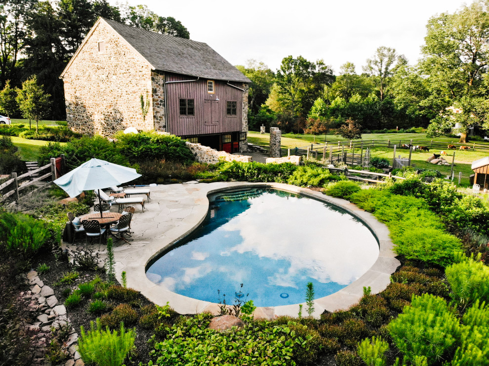 Inspiration for a mid-sized country backyard kidney-shaped natural pool in Philadelphia with a pool house and natural stone pavers.