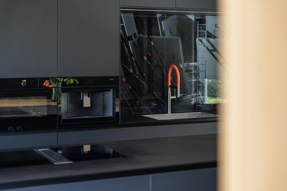 Inspiration pour une très grande cuisine ouverte parallèle design avec un placard à porte plane, des portes de placard noires, un plan de travail en stratifié, une crédence en feuille de verre, un électroménager noir, îlot et plan de travail noir.