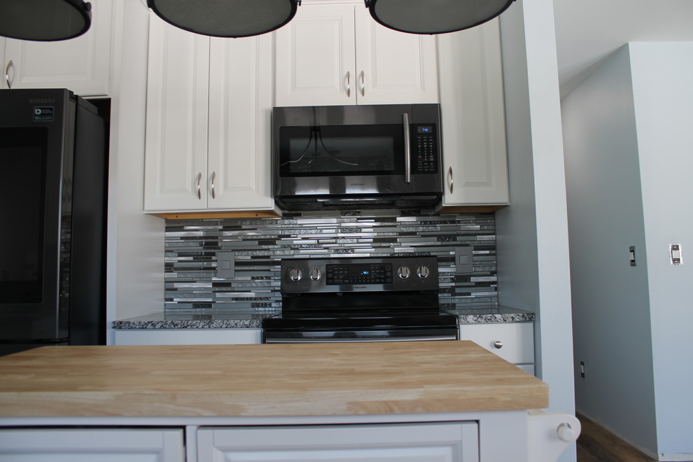 Example of a mid-sized transitional u-shaped dark wood floor and brown floor kitchen design with an undermount sink, raised-panel cabinets, white cabinets, granite countertops, multicolored backsplash, matchstick tile backsplash, stainless steel appliances and an island