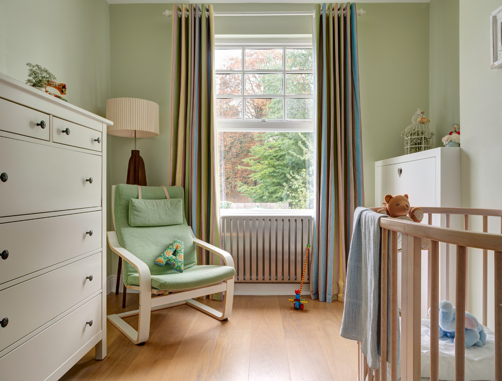 This is an example of a mid-sized traditional gender-neutral nursery in London with green walls and light hardwood floors.