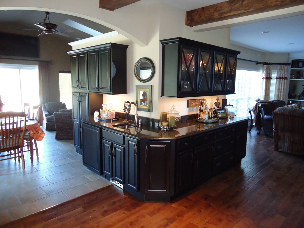 Photo of a mid-sized country single-wall eat-in kitchen in St Louis with a drop-in sink, glass-front cabinets, black cabinets, quartz benchtops, dark hardwood floors, no island and brown floor.