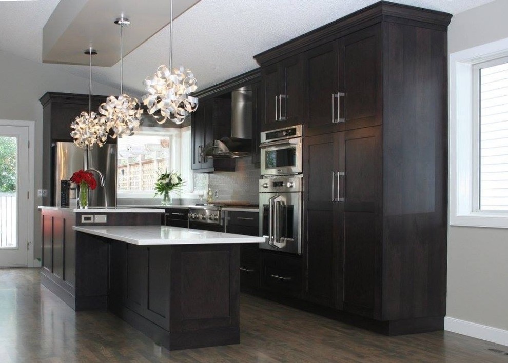 Open concept kitchen - mid-sized transitional l-shaped dark wood floor open concept kitchen idea in Calgary with a triple-bowl sink, shaker cabinets, dark wood cabinets, quartz countertops, gray backsplash, glass tile backsplash, stainless steel appliances and an island