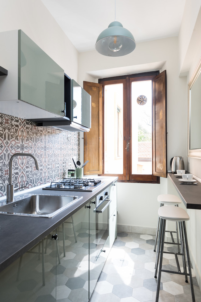 This is an example of a small mediterranean kitchen in Rome with a drop-in sink, flat-panel cabinets, green cabinets, multi-coloured splashback, stainless steel appliances, multi-coloured floor and black benchtop.