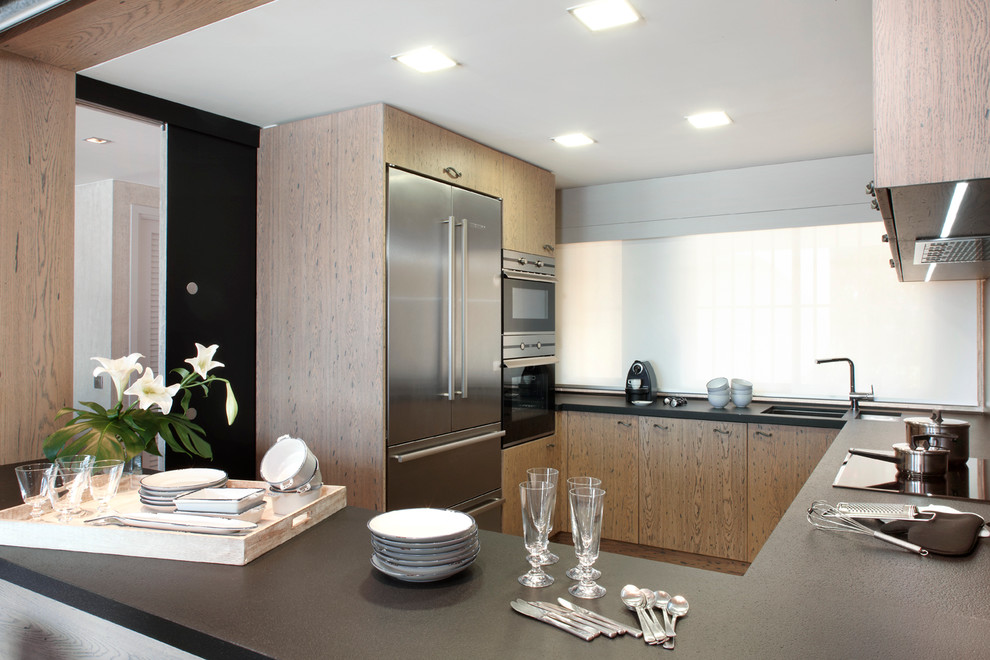 Photo of a mid-sized contemporary u-shaped separate kitchen in Barcelona with an undermount sink, flat-panel cabinets, medium wood cabinets, solid surface benchtops, stainless steel appliances and no island.
