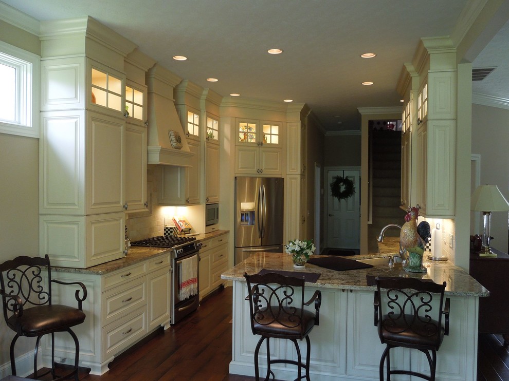 Inspiration for a large u-shaped porcelain tile eat-in kitchen remodel with a double-bowl sink, raised-panel cabinets, beige cabinets, granite countertops, beige backsplash, cement tile backsplash, stainless steel appliances and a peninsula