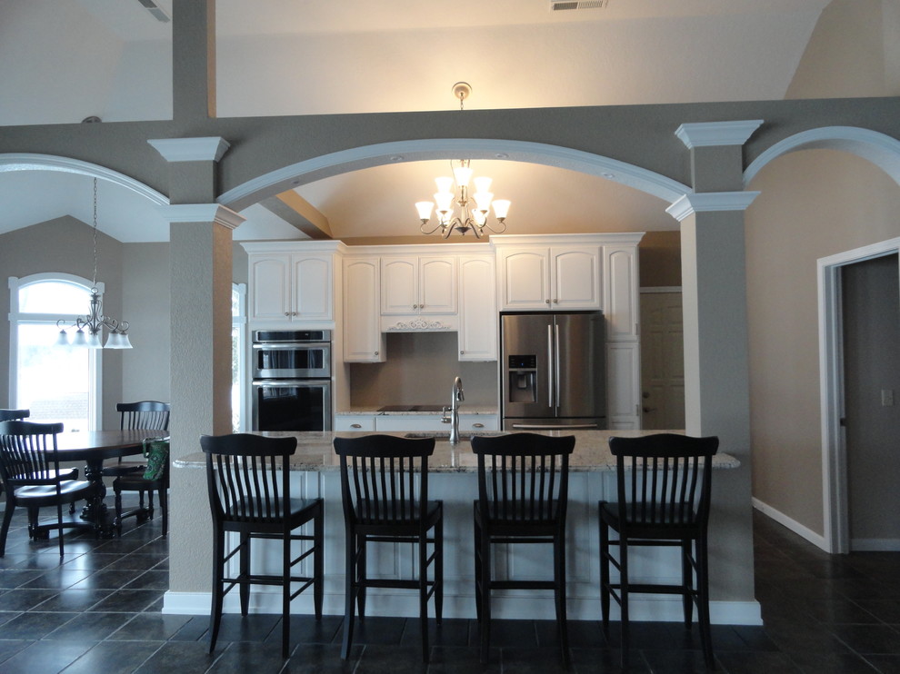 Mid-sized transitional galley porcelain tile and black floor open concept kitchen photo with a single-bowl sink, raised-panel cabinets, white cabinets, granite countertops, stainless steel appliances and an island