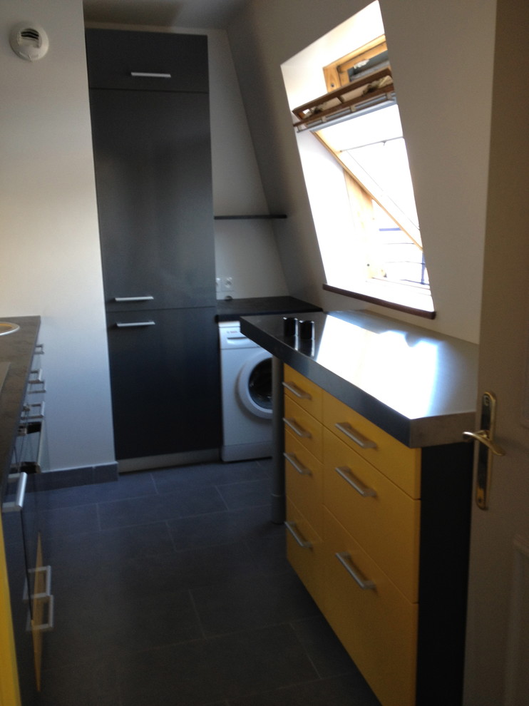 Photo of a small modern galley separate kitchen in Lyon with an undermount sink, flat-panel cabinets, yellow cabinets, stainless steel benchtops, yellow splashback, glass sheet splashback, black appliances, ceramic floors, no island, grey floor and black benchtop.