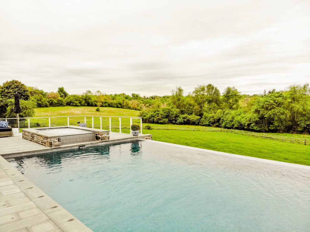 На фото: большой прямоугольный бассейн-инфинити на заднем дворе в современном стиле с домиком у бассейна и покрытием из каменной брусчатки