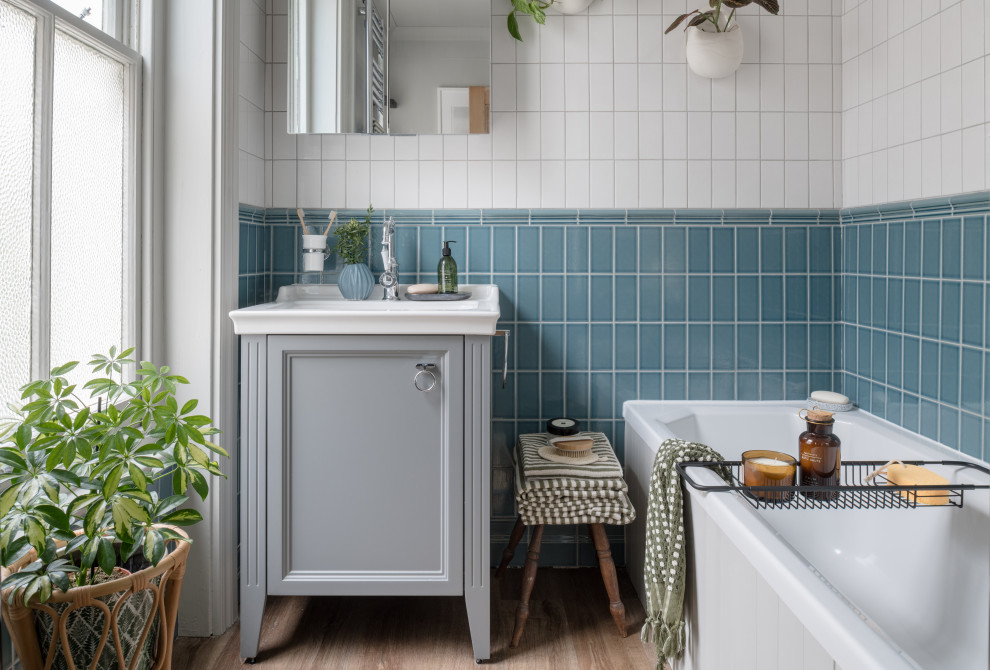 Design ideas for a small classic grey and white bathroom in Sussex with shaker cabinets, grey cabinets, a built-in bath, blue tiles, ceramic tiles, grey walls, laminate floors, a submerged sink, solid surface worktops, brown floors, white worktops, a dado rail, a single sink and a freestanding vanity unit.