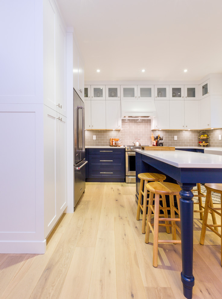 Example of a large transitional u-shaped light wood floor open concept kitchen design with a farmhouse sink, shaker cabinets, blue cabinets, quartz countertops, gray backsplash, glass tile backsplash, stainless steel appliances, an island and white countertops