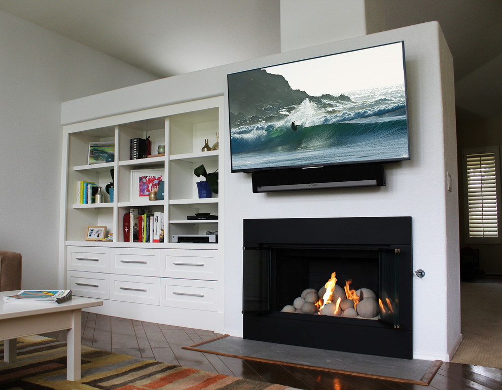 This is an example of a mid-sized scandinavian open concept family room in San Diego with white walls, dark hardwood floors, a standard fireplace, a metal fireplace surround and a wall-mounted tv.