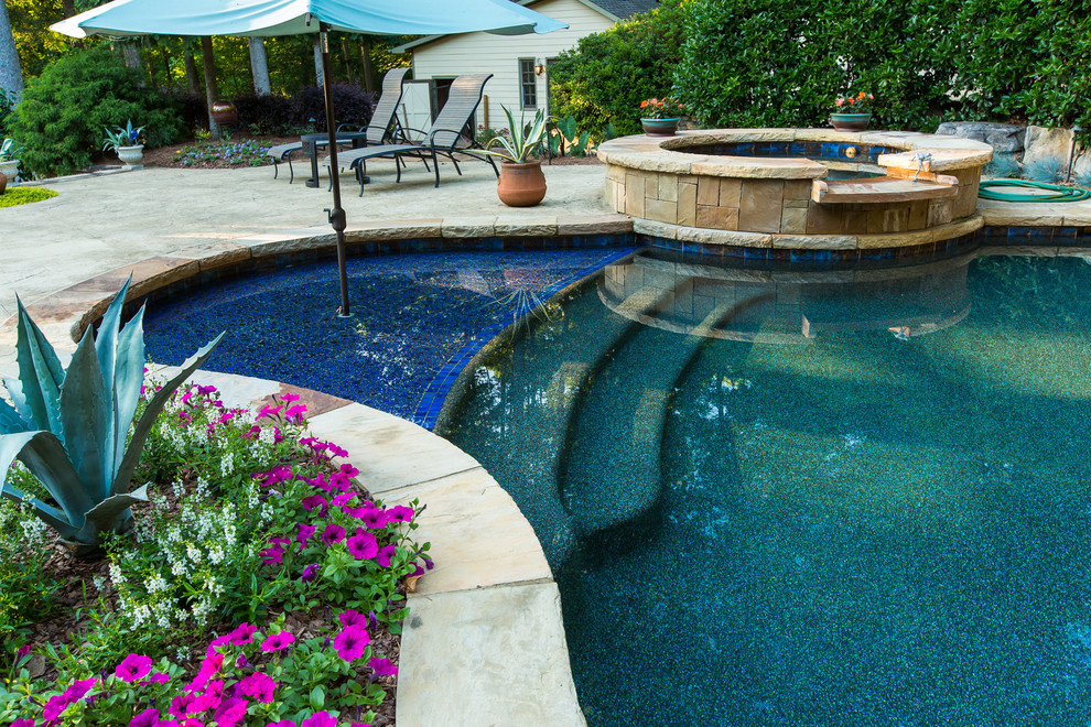 This is an example of a large tropical backyard custom-shaped natural pool in Atlanta with stamped concrete and a hot tub.