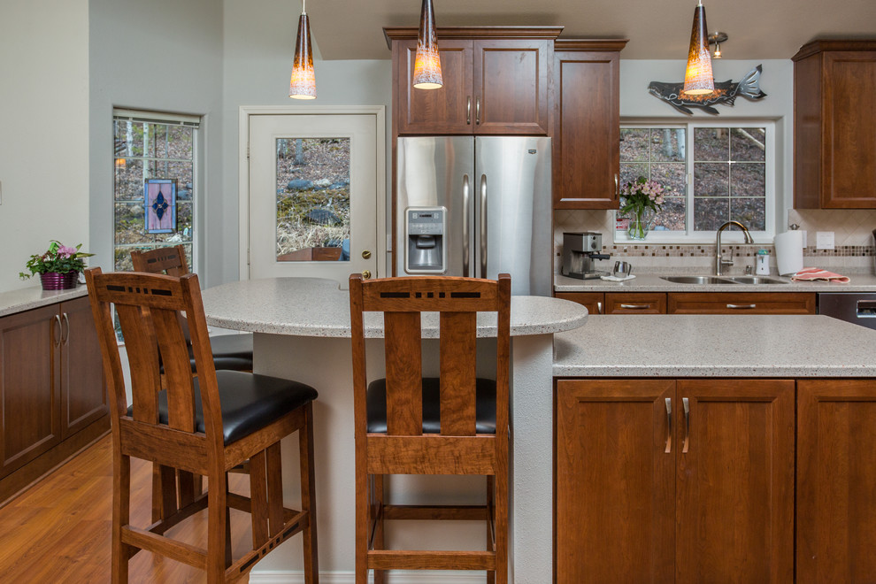 Example of a mid-sized transitional u-shaped medium tone wood floor kitchen pantry design with an undermount sink, recessed-panel cabinets, medium tone wood cabinets, solid surface countertops, beige backsplash, mosaic tile backsplash, stainless steel appliances and an island