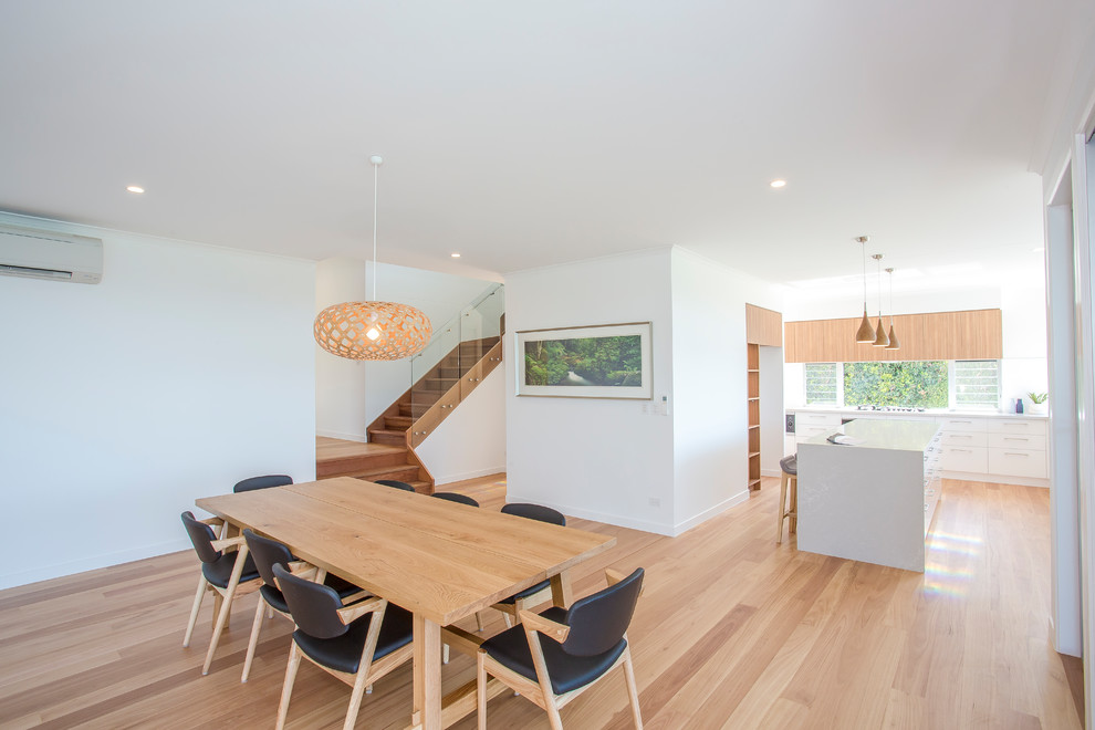 Large contemporary open plan dining in Sunshine Coast with white walls, light hardwood floors, no fireplace and brown floor.