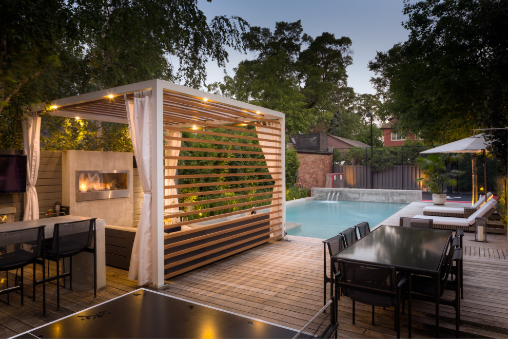 This is an example of a mid-sized industrial backyard patio in Toronto with with fireplace, decking and a pergola.