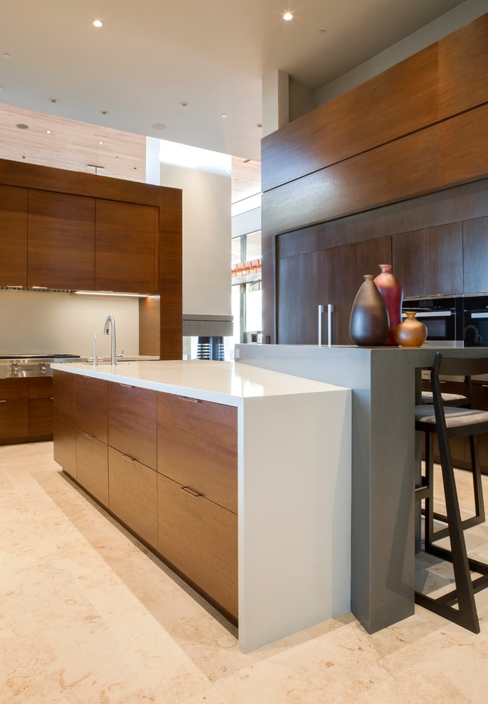 This is an example of a large modern u-shaped eat-in kitchen in Phoenix with a drop-in sink, flat-panel cabinets, medium wood cabinets, onyx benchtops, beige splashback, ceramic splashback, panelled appliances, limestone floors, with island and beige floor.