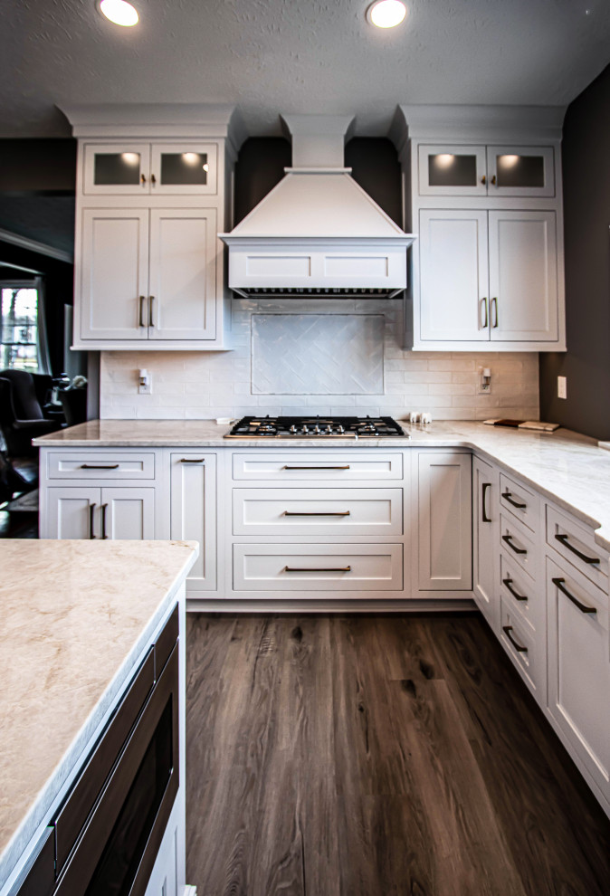 Eat-in kitchen - mid-sized transitional u-shaped vinyl floor and brown floor eat-in kitchen idea in Cleveland with a farmhouse sink, flat-panel cabinets, white cabinets, quartz countertops, white backsplash, ceramic backsplash, stainless steel appliances, an island and beige countertops