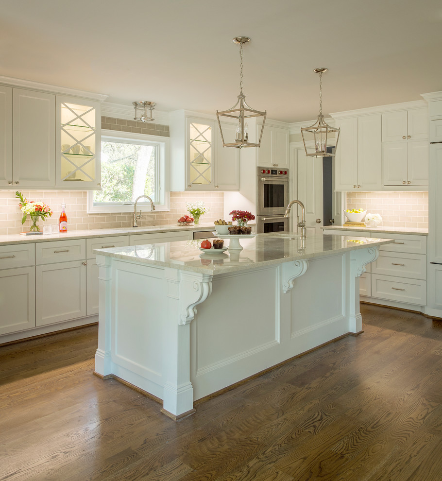 This is an example of a traditional kitchen in Houston with an undermount sink, shaker cabinets, white cabinets, quartzite benchtops, beige splashback, subway tile splashback, stainless steel appliances, dark hardwood floors, with island, brown floor and beige benchtop.