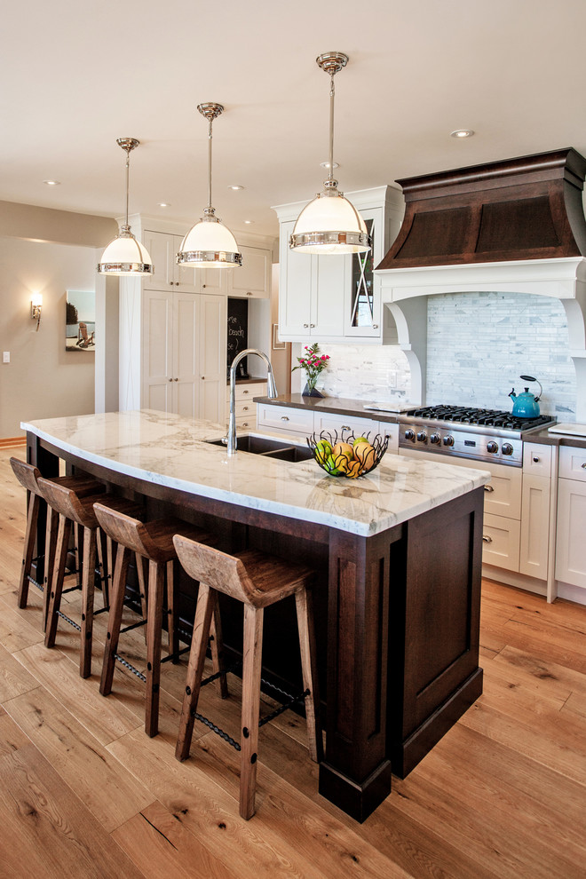 Photo of a large beach style l-shaped eat-in kitchen in Toronto with an undermount sink, shaker cabinets, white cabinets, quartz benchtops, white splashback, matchstick tile splashback, stainless steel appliances, light hardwood floors and with island.