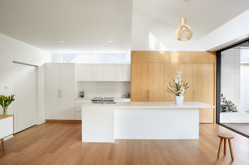 This is an example of a mid-sized contemporary open plan kitchen in Melbourne with an undermount sink, white splashback, light hardwood floors and with island.