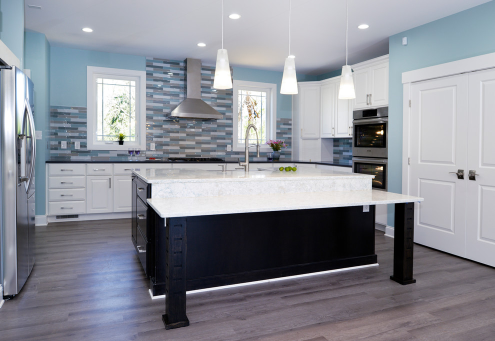 Inspiration for a mid-sized transitional u-shaped separate kitchen in Orange County with a farmhouse sink, raised-panel cabinets, white cabinets, solid surface benchtops, multi-coloured splashback, glass tile splashback, stainless steel appliances, dark hardwood floors and with island.