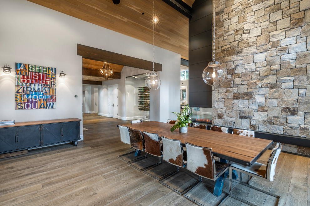 Exemple d'une grande salle à manger chic avec un mur gris, un sol en bois brun, une cheminée double-face, un manteau de cheminée en métal, un sol marron et un plafond en bois.
