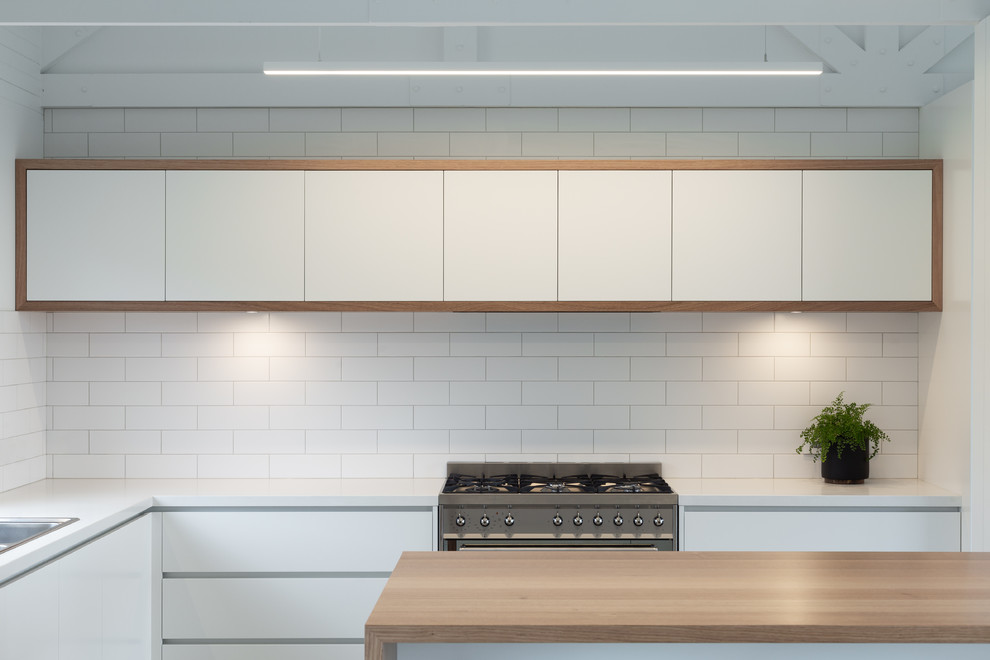 Inspiration for a mid-sized country l-shaped kitchen in Hobart with a drop-in sink, flat-panel cabinets, white cabinets, wood benchtops, white splashback, subway tile splashback, stainless steel appliances, with island and beige benchtop.