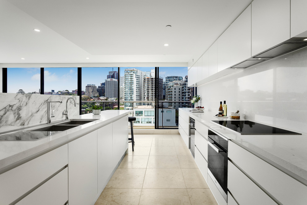 Inspiration for a contemporary galley kitchen in Sydney with an undermount sink, flat-panel cabinets, white cabinets, white splashback, black appliances, with island, beige floor and white benchtop.