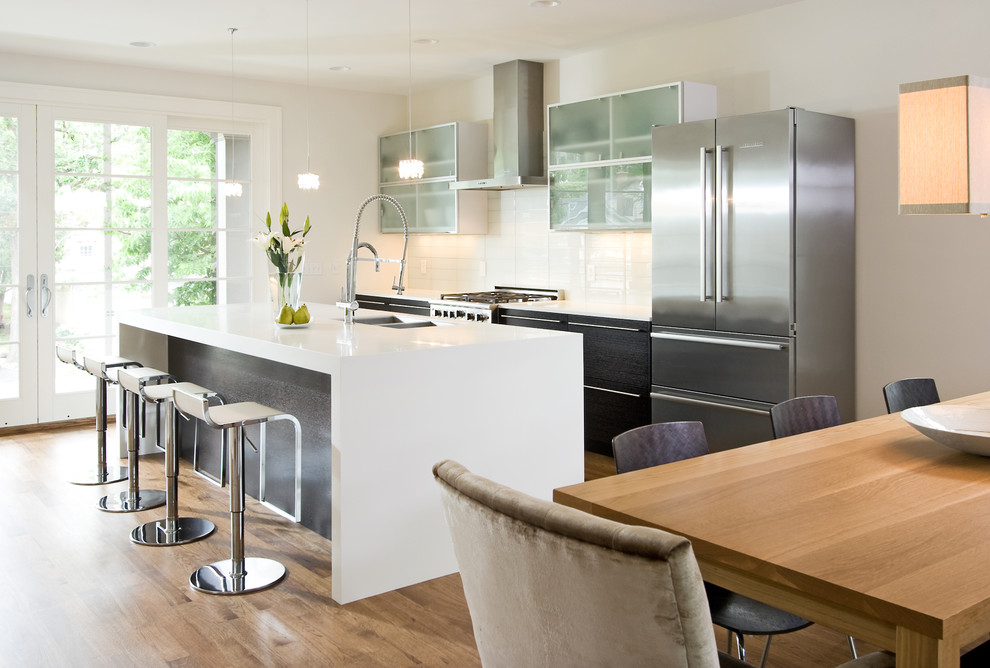 Modern kitchen in Minneapolis with flat-panel cabinets, black cabinets, white splashback and stainless steel appliances.