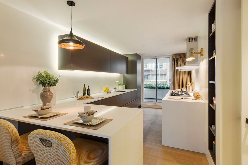 Mid-sized contemporary u-shaped separate kitchen in Barcelona with flat-panel cabinets, brown cabinets, white splashback, medium hardwood floors, a peninsula, brown floor, white benchtop and an undermount sink.