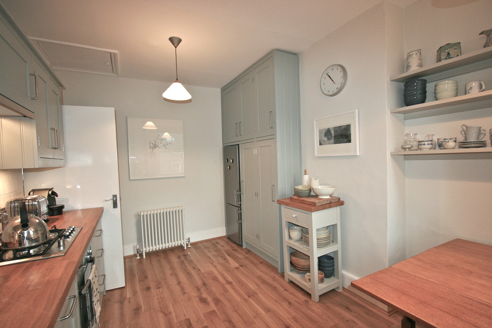 Small contemporary galley eat-in kitchen in London with a drop-in sink, shaker cabinets, green cabinets, wood benchtops, white splashback, ceramic splashback, stainless steel appliances, medium hardwood floors and no island.