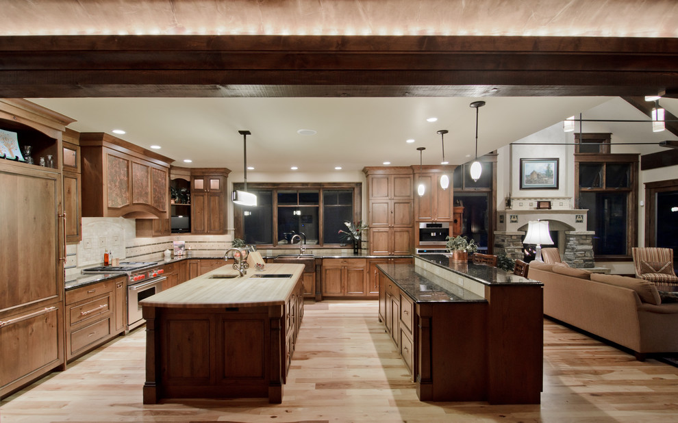 This is an example of a traditional l-shaped open plan kitchen in Denver with panelled appliances, dark wood cabinets and multiple islands.