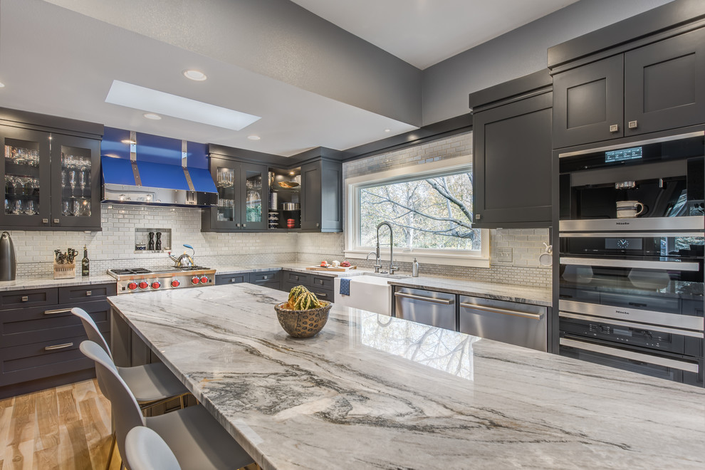 Inspiration for a large transitional u-shaped light wood floor eat-in kitchen remodel in Denver with a farmhouse sink, recessed-panel cabinets, gray cabinets, quartzite countertops, blue backsplash, ceramic backsplash, stainless steel appliances and an island