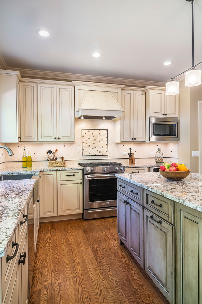 Example of a transitional l-shaped medium tone wood floor eat-in kitchen design in Chicago with a farmhouse sink, raised-panel cabinets, distressed cabinets, granite countertops, multicolored backsplash, ceramic backsplash, stainless steel appliances and an island