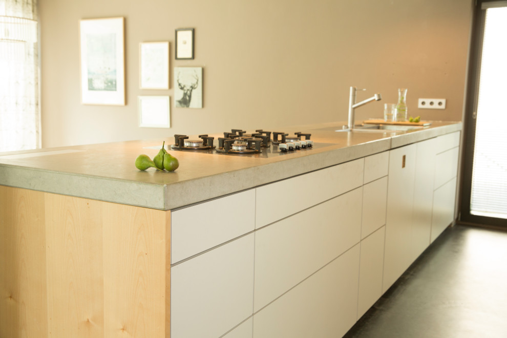 Inredning av ett stort grå grått kök, med en nedsänkt diskho, släta luckor, vita skåp, bänkskiva i kalksten, betonggolv, en halv köksö och svart golv