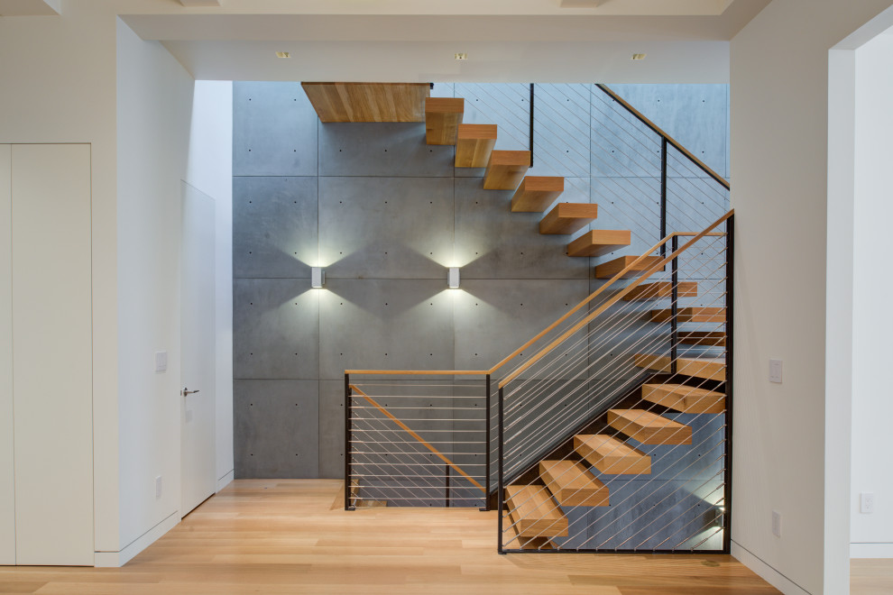 Стильный дизайн: лестница на больцах, среднего размера в стиле модернизм с деревянными ступенями, перилами из тросов и панелями на части стены без подступенок - последний тренд