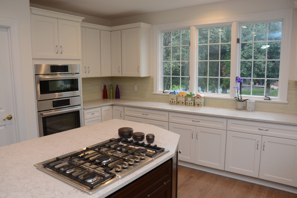 This is an example of a large traditional u-shaped open plan kitchen in DC Metro with an undermount sink, recessed-panel cabinets, white cabinets, quartz benchtops, grey splashback, mosaic tile splashback, stainless steel appliances, light hardwood floors, with island, brown floor and white benchtop.