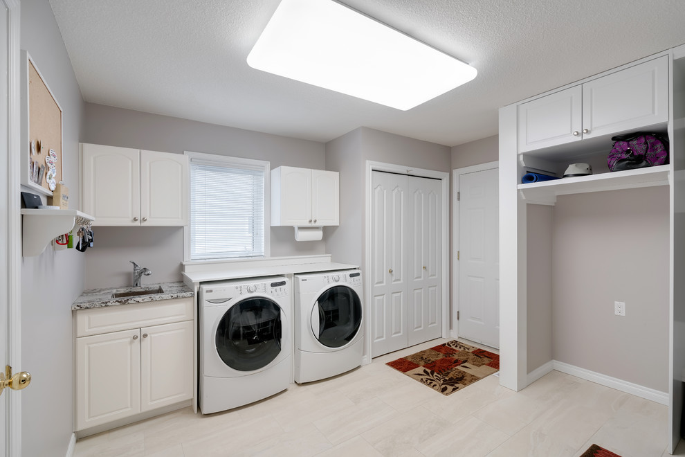 Mid-sized modern u-shaped utility room in Edmonton with an undermount sink, shaker cabinets, white cabinets, grey walls, a side-by-side washer and dryer and white floor.