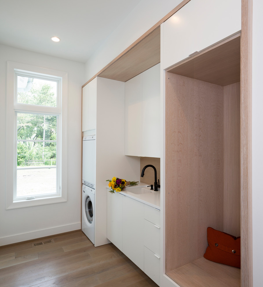 Design ideas for a contemporary laundry room in Minneapolis with an undermount sink, flat-panel cabinets, white cabinets, beige splashback, white walls, a stacked washer and dryer and white benchtop.