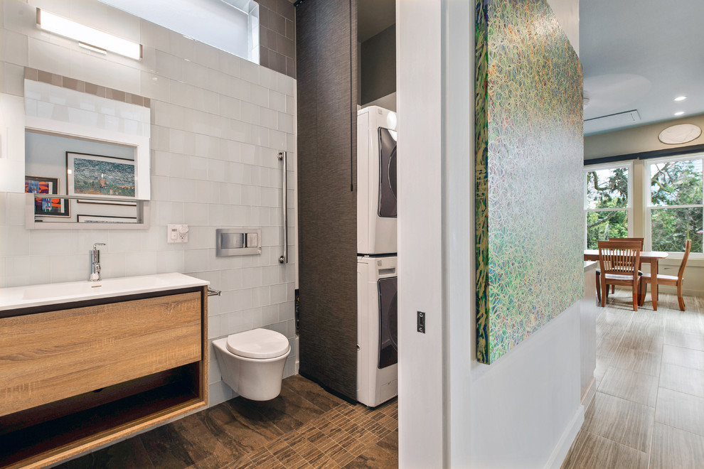 This is an example of a mid-sized contemporary 3/4 bathroom in San Francisco with flat-panel cabinets, light wood cabinets, a wall-mount toilet, white tile, glass tile, white walls, travertine floors, an integrated sink, solid surface benchtops, a single vanity, a floating vanity and a laundry.